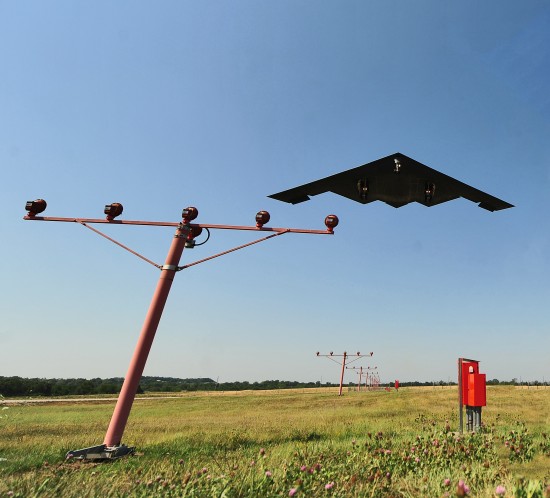 A stealth bomber flies over airport approach lights at Whiteman AFB