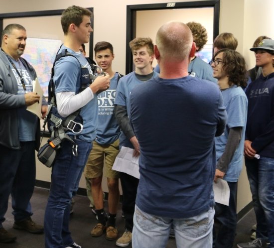 A students dons a tower climber safety harness at Manufacturing Day 2018